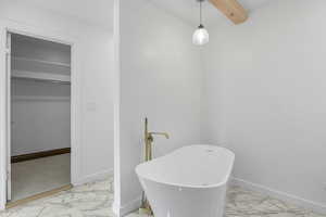 Full bath with light marble finish flooring, a freestanding tub, a walk in closet, and beam ceiling