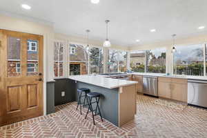 Kitchen featuring brick floors, a breakfast bar area, a peninsula, dishwasher, and ornamental molding