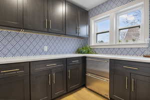 Kitchen featuring dark brown cabinets, light wood-style flooring, light stone counters, and stainless steel dishwasher