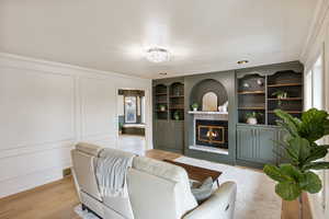 Living room with a glass covered fireplace, a decorative wall, light wood finished floors, and built in features