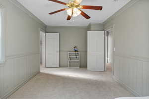 Unfurnished bedroom featuring crown molding, carpet, ceiling fan, and wainscoting