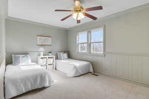 Bedroom featuring wainscoting, crown molding, carpet, and ceiling fan