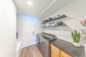 Laundry area with separate washer and dryer, light wood-type flooring, and cabinet space
