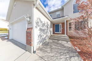 View of exterior entry featuring a porch, an attached garage, driveway, brick siding, and stucco siding