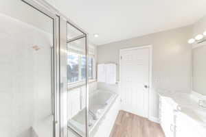 Full bath featuring vanity, a shower stall, a garden tub, and light wood-style floors
