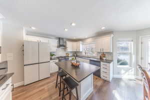 Kitchen with a kitchen bar, wall chimney exhaust hood, appliances with stainless steel finishes, a kitchen island, and dark wood-style floors