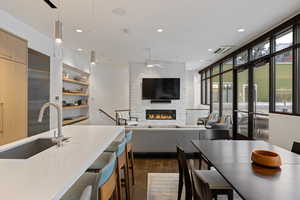 Kitchen featuring a stone fireplace, decorative light fixtures, dark wood-style flooring, ceiling fan, and modern cabinets