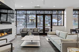 Living room with floor to ceiling windows, a stone fireplace, and wood finished floors