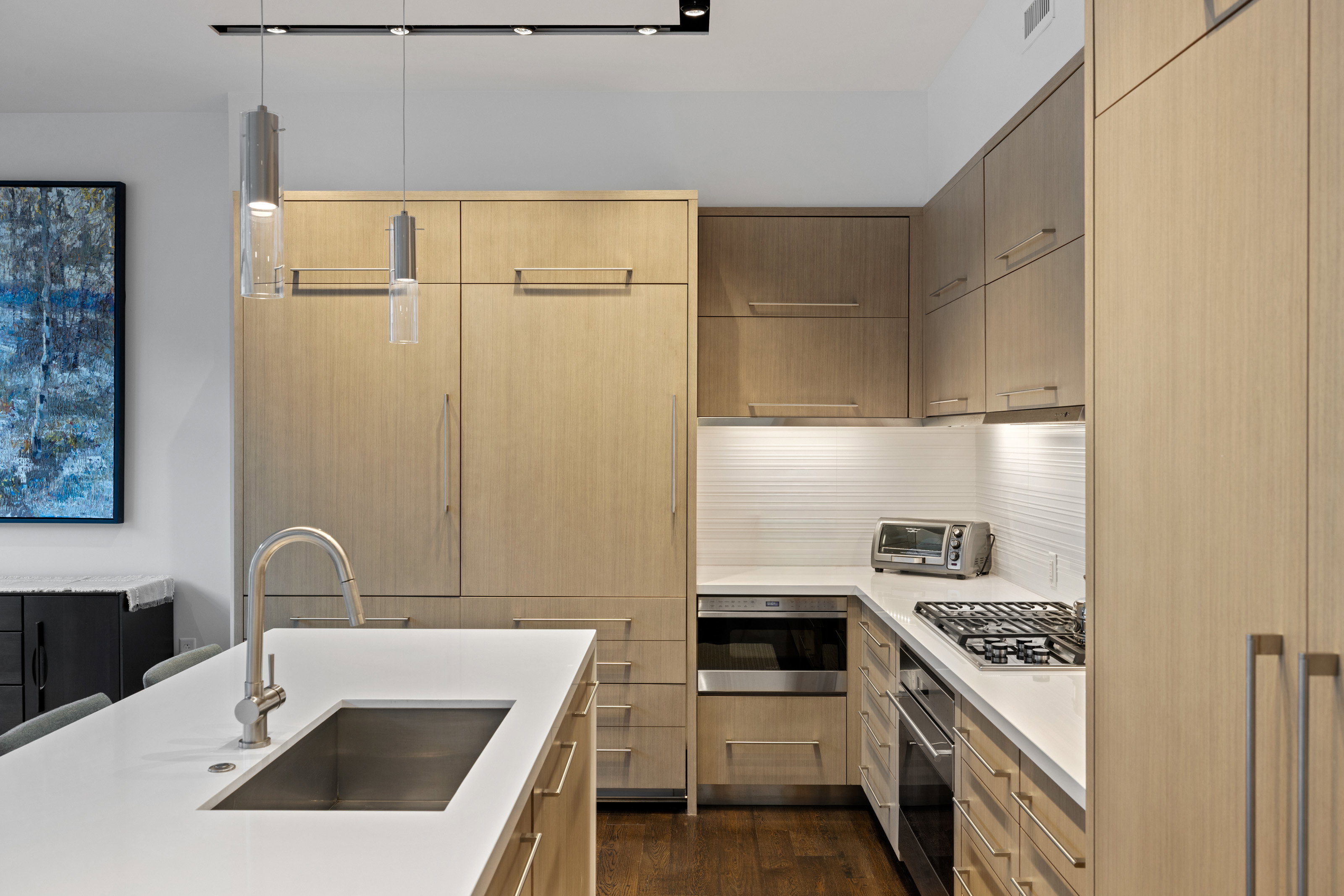 Kitchen featuring hanging light fixtures, modern cabinets, stainless steel appliances, dark wood finished floors, and light stone countertops