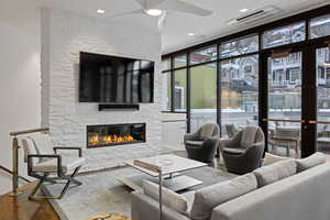 Living room featuring ceiling fan, a stone fireplace, and wood finished floors