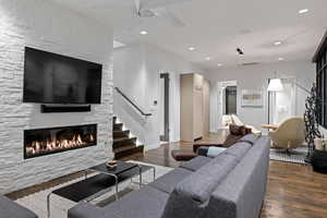 Living area featuring stairs, dark wood-type flooring, a ceiling fan, a fireplace, and recessed lighting