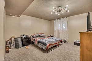 Bedroom featuring a textured ceiling, carpet floors, and a chandelier