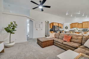Living area with arched walkways, light carpet, high vaulted ceiling, and ceiling fan