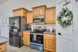 Kitchen featuring appliances with stainless steel finishes, light brown cabinetry, light tile patterned flooring, and dark countertops