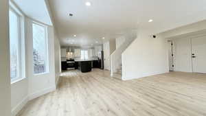 Unfurnished living room featuring light wood-style floors, recessed lighting, and stairway