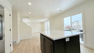 Kitchen featuring dark cabinets, a center island, light wood finished floors, open floor plan, and recessed lighting
