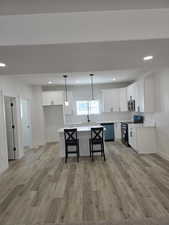 Kitchen with range with electric cooktop, white cabinets, light wood-style floors, and dishwashing machine