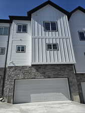 View of front of property featuring board and batten siding, stone siding, driveway, and a garage