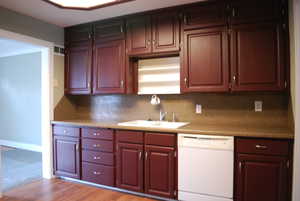 Kitchen with white dishwasher, light countertops, dark wood-style floors, and backsplash