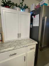 Kitchen view of freestanding refrigerator, white cabinets, and light stone counters