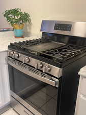 Kitchen view of stainless steel gas range, light stone countertops, and white cabinets