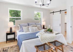 Bedroom with a barn door, a chandelier, and light wood-style flooring