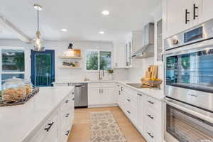Kitchen with stainless steel appliances, decorative light fixtures, white cabinetry, wall chimney exhaust hood, and recessed lighting