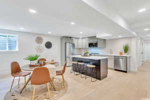 Kitchen featuring a kitchen bar, a kitchen island, stainless steel appliances, light wood-type flooring, and recessed lighting