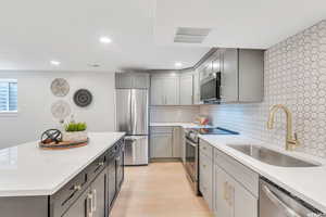 Kitchen with stainless steel appliances, a kitchen island, gray cabinets, light stone countertops, and recessed lighting