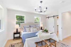 Bedroom with a barn door, light wood-style floors, and a chandelier