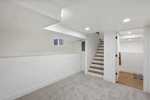 Finished basement featuring light colored carpet, stairs, recessed lighting, and electric panel