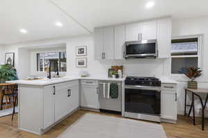 Kitchen featuring stainless steel appliances, recessed lighting, a peninsula, light wood-type flooring, and white cabinetry
