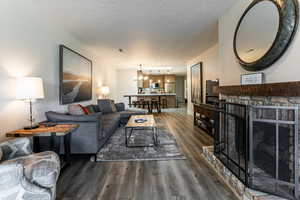 Living area featuring a stone fireplace, a chandelier, dark wood-style flooring, and a textured ceiling