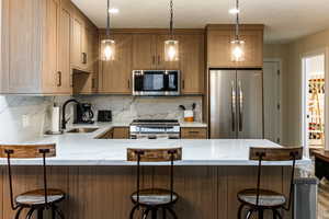 Kitchen featuring appliances with stainless steel finishes, light stone counters, pendant lighting, and a breakfast bar area
