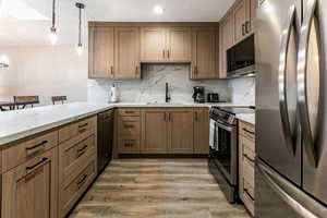 Kitchen featuring appliances with stainless steel finishes, hanging light fixtures, brown cabinetry, and light wood-style floors