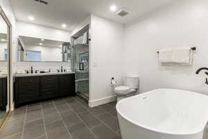 Bathroom featuring a freestanding tub, double vanity, a stall shower, dark tile patterned flooring, and recessed lighting