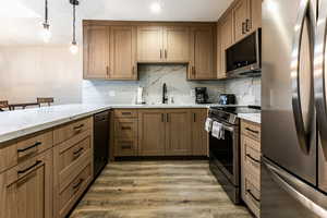Kitchen featuring appliances with stainless steel finishes, brown cabinetry, pendant lighting, light wood-style floors, and light stone counters