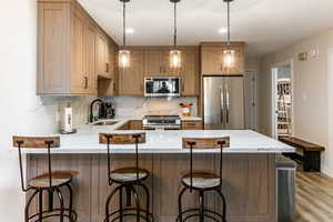 Kitchen featuring stainless steel appliances, light stone countertops, a peninsula, brown cabinets, and hanging light fixtures