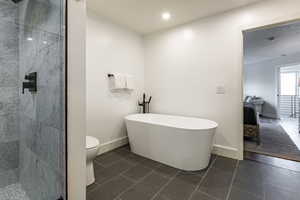 Bathroom featuring a freestanding tub, a marble finish shower, and dark tile patterned floors