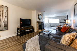 Living room with a textured ceiling, dark wood finished floors, and a brick fireplace