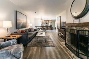 Living area with dark wood-type flooring, a textured ceiling, a chandelier, and a brick fireplace