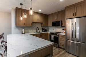 Kitchen featuring stainless steel appliances, a peninsula, light stone counters, brown cabinets, and dark wood finished floors