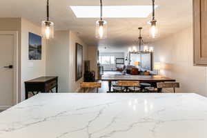 Kitchen featuring light stone countertops, hanging light fixtures, a chandelier, a textured ceiling, and a skylight
