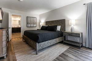 Bedroom with wood finished floors, a textured ceiling, and ensuite bath