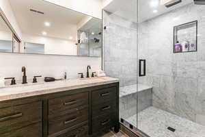 Full bath with double vanity, a shower stall, and recessed lighting