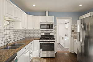 Kitchen featuring appliances with stainless steel finishes, washing machine and clothes dryer, white cabinetry, backsplash, and dark wood-style flooring