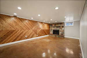 Unfurnished living room with finished concrete flooring, a stone fireplace, recessed lighting, and wood walls