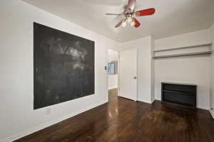 Unfurnished living room featuring a ceiling fan and dark wood-type flooring