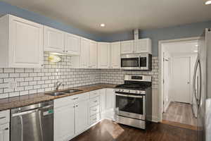 Kitchen with appliances with stainless steel finishes, white cabinets, dark stone counters, dark wood finished floors, and recessed lighting