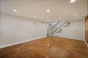 Unfurnished living room featuring recessed lighting, finished concrete flooring, and stairs